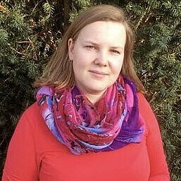 Leiterin des Kindergartens Am Wald- Klinikum Aline Greulich vor einem Baum Aline Greulich, Leiterin, vor Baum, trägt ein rotes Langarmshirt und ein lilanes Tuch, hat halblange braune offene Haare