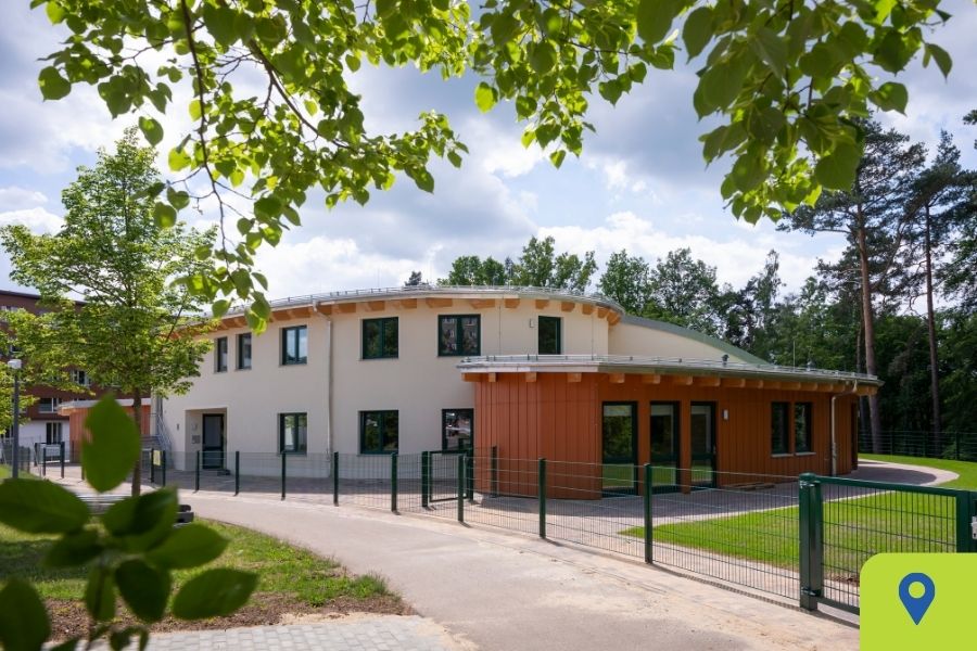 Der Kindergarten von außen, mit einem Baum im Vordergrund Gebäude, Kindergarten, mit Bäumen im Vordergrund, Zaun, Weg