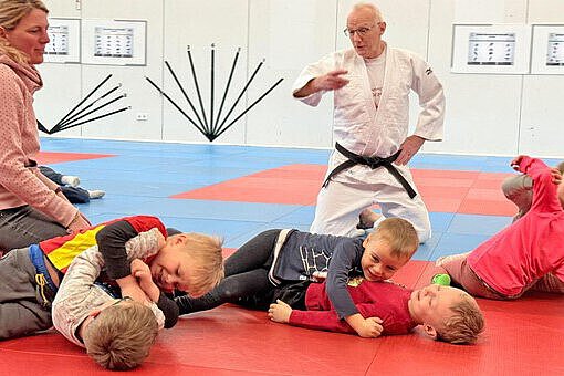 Judo-Training mit Kindern in der Kita Sportforum Kinder üben gemeinsam spielerische Judo-Bewegungen auf einer roten und blauen Matte, angeleitet vom Trainer im Judogi.