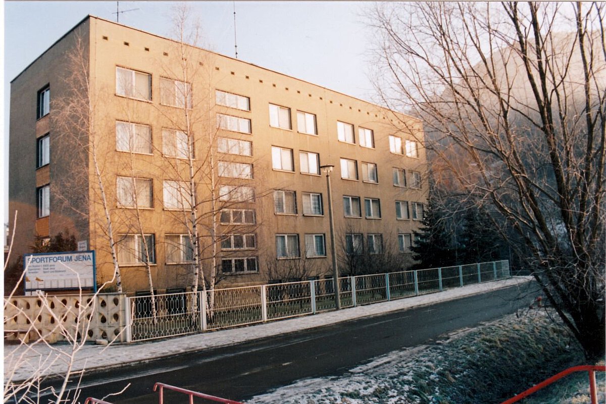 Akademiehotel Jena 1995 – Gebäude am Sportforum im Winter Mehrstöckiges Gebäude des Sportforums Jena im Winter 1995 mit Straßenansicht, kahlen Bäumen und leichter Schneeschicht